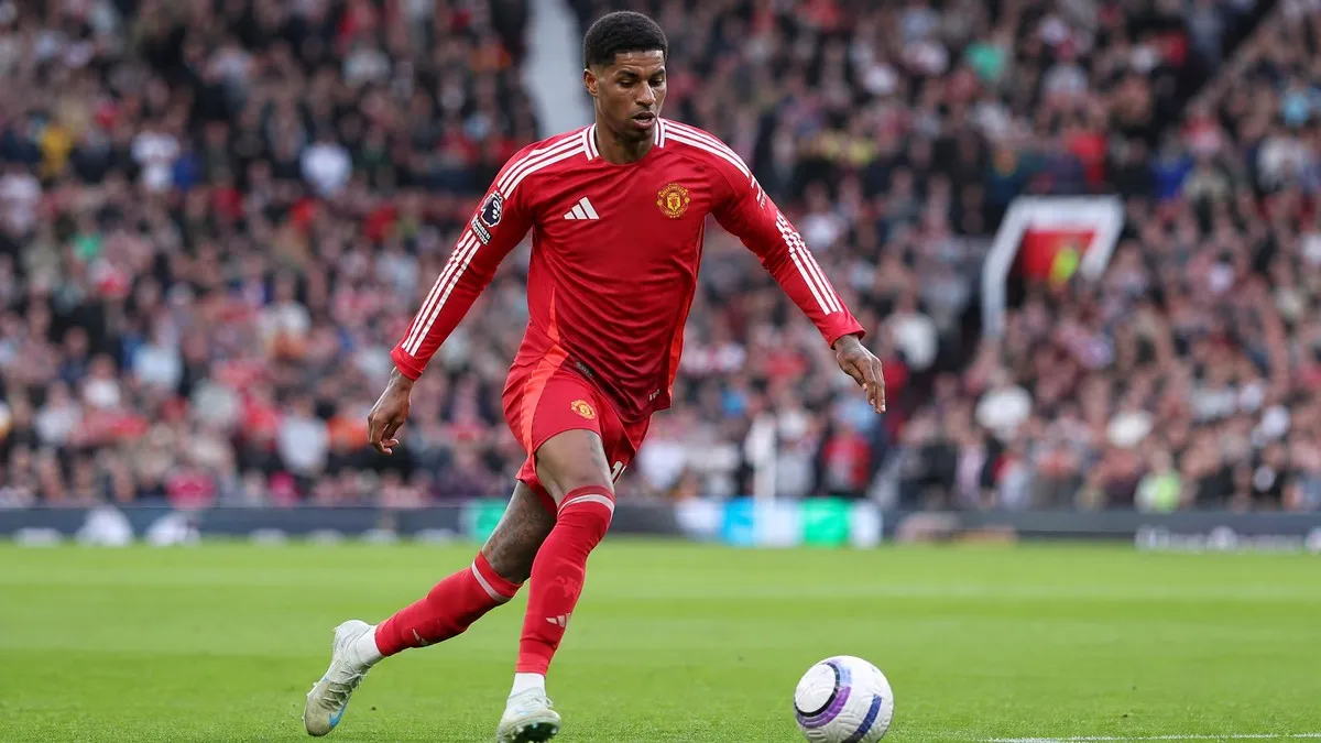 Marcus Rashford in a red Manchester United home kit, captured mid-stride on a football pitch, demonstrating agility and focus.