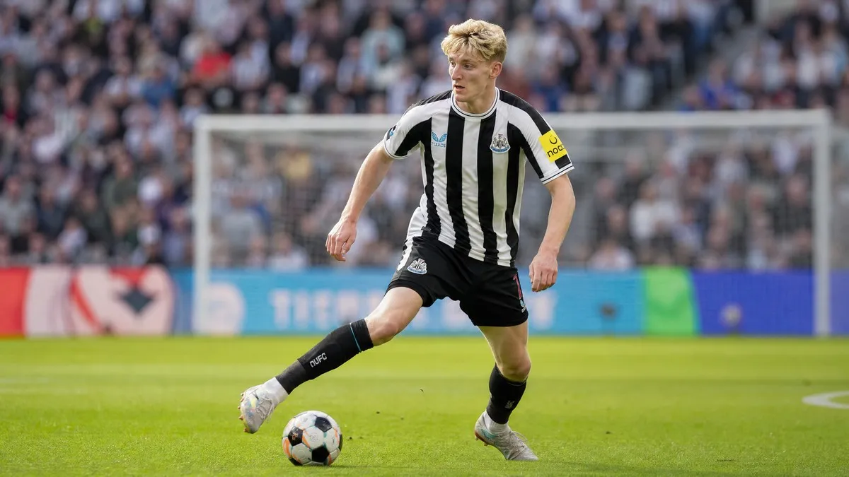 Anthony Gordon in Newcastle United's black and white striped home kit, dribbling a football on a green pitch during a Premier League match.