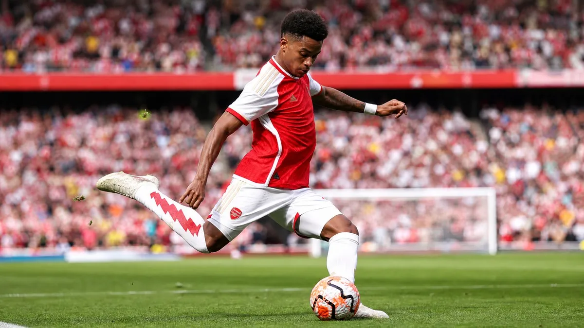Bukayo Saka in action, wearing his red and white Arsenal kit, striking a football on a stadium pitch during a Premier League match.