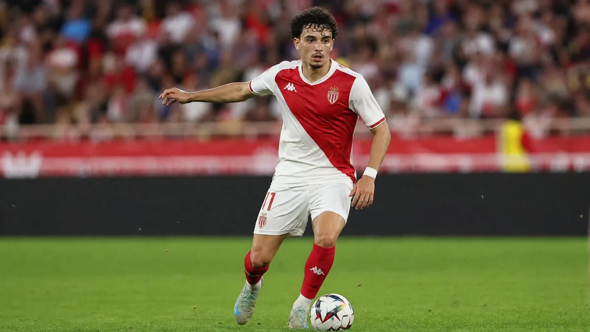 Maghnes Akliouche in action wearing his AS Monaco home kit, dribbling the ball on the pitch during a Ligue 1 match.